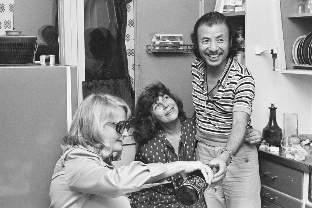 Randi Hultin i lystig lag med sangeren Karin Krog og den japanske saxofonisten Sadao Watanabe, på kjøkkenet i Gartnerveien, 28. august 1975. Foto: Randi Hultin/Nasjonalbiblioteket