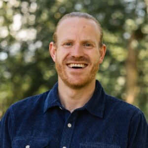 Mann med litt skjegg og bart smiler til kamera.